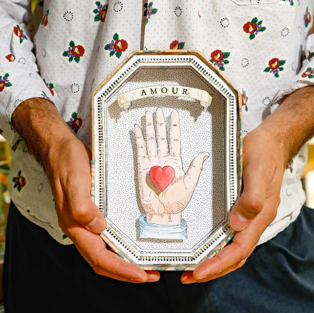 "Hand-painted Octagon Amour Shadow Box by Marin Montagut, featuring the word 'Amour' in a romantic design inside a glass-enclosed papier-mâché display, handcrafted in Paris. Dimensions: 8.46x5.59x1.85 inches."